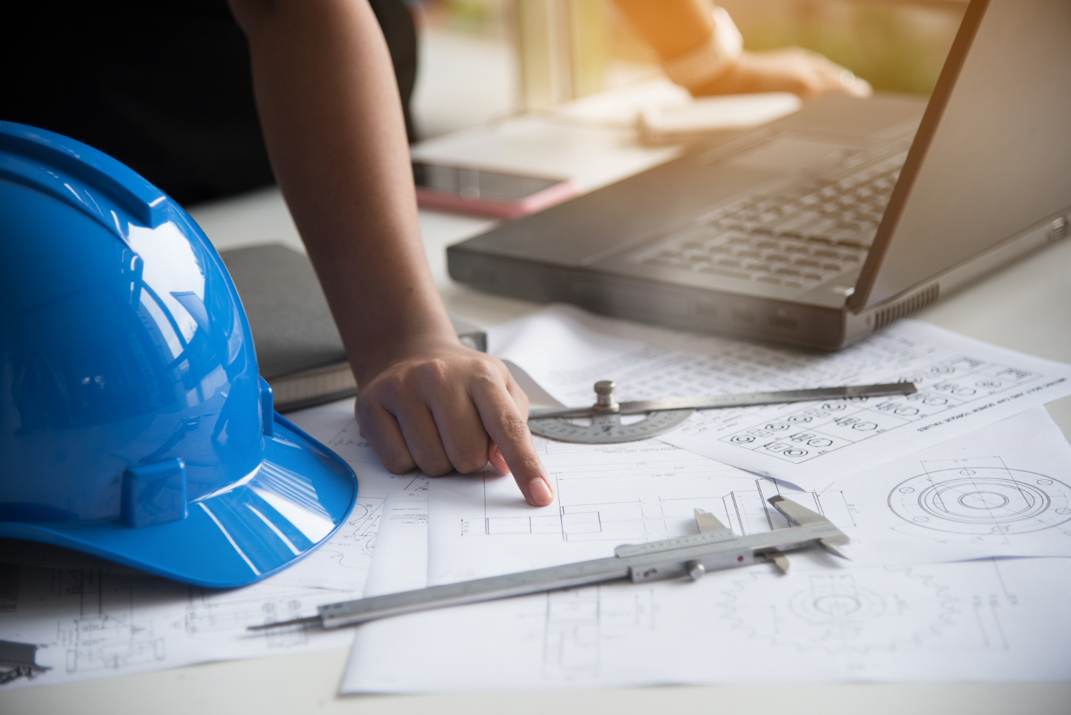 Hand showing something on paper and an engineer helmet on the side