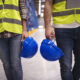 two unrecognizable workers reflective suit walking through warehouse holding blue protective hardhats scaled